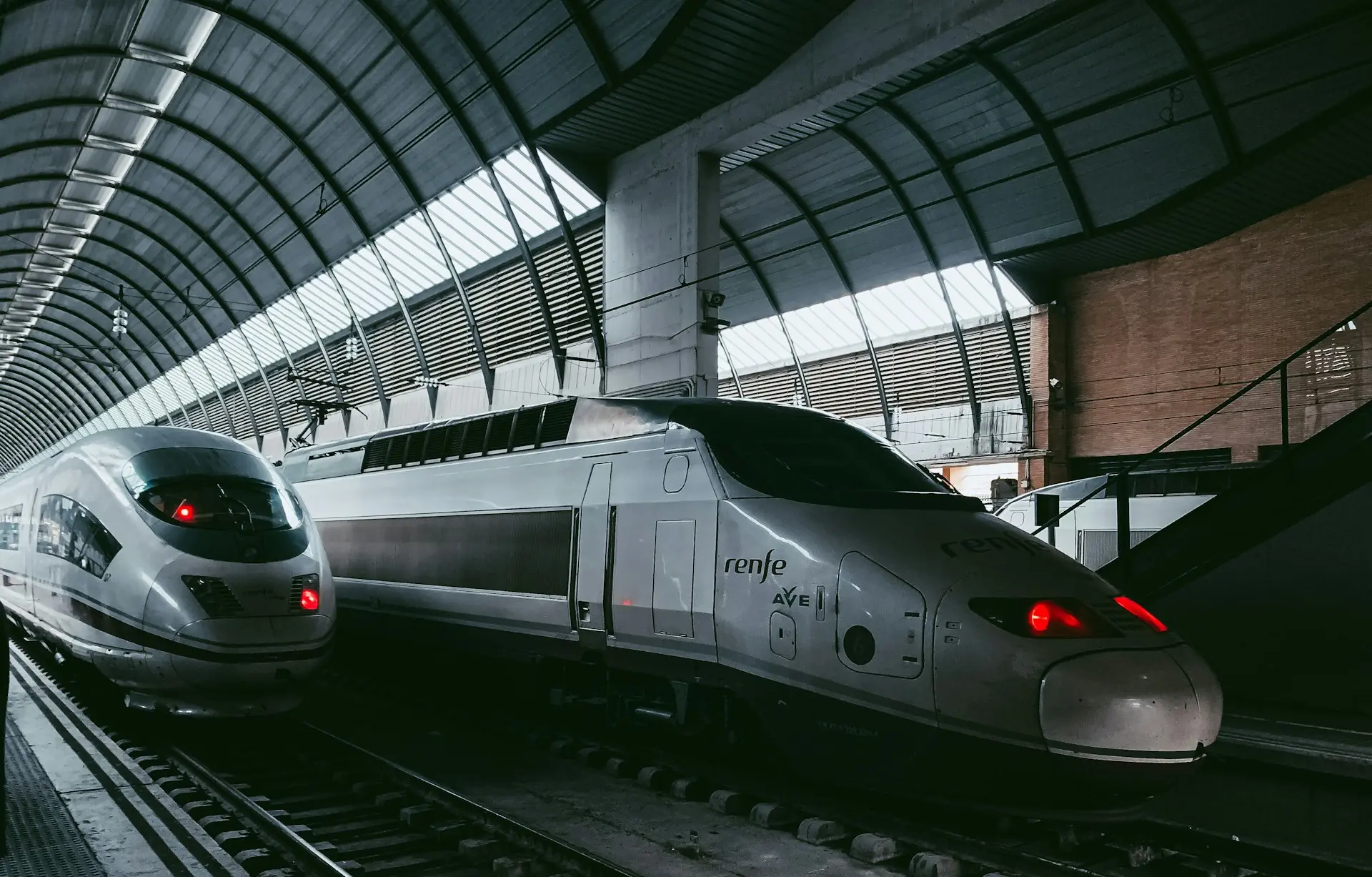 a silver train traveling down train tracks next to a loading platform
